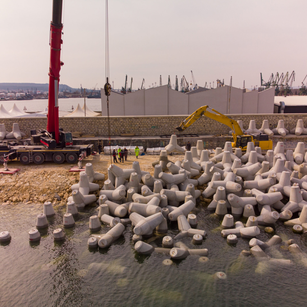 Aerial top view of breakwater construction. Bulldozer and crane on a pile of boulders in the sea