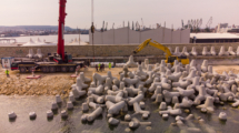 Aerial top view of breakwater construction. Bulldozer and crane on a pile of boulders in the sea