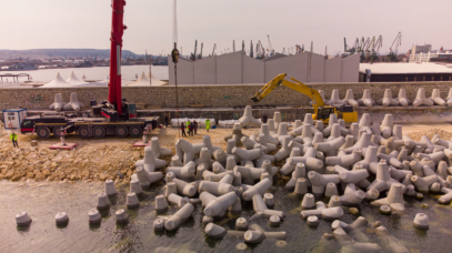 Aerial top view of breakwater construction. Bulldozer and crane on a pile of boulders in the sea