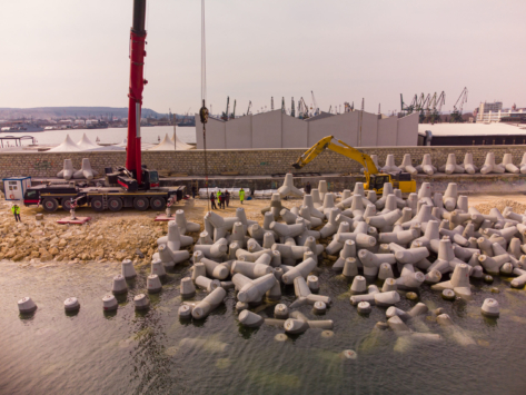Aerial top view of breakwater construction. Bulldozer and crane on a pile of boulders in the sea